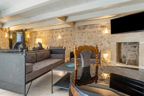 A stone-walled room with a sofa, a wooden chair, a fireplace, and a television. - GuestHost - Charming 65 sqm apartment, tastefully furnished and perfect for a stay for two. Located on the ground floor of a characteristic building, the accommodation was created from the ancient caves of Modica and transformed into a charming two-level (Modica)