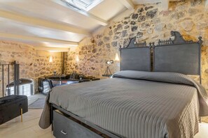 A bedroom with a stone wall, a bed with a headboard, a bench, a sink, and a hanging light fixture. - GuestHost - Charming 65 sqm apartment, tastefully furnished and perfect for a stay for two. Located on the ground floor of a characteristic building, the accommodation was created from the ancient caves of Modica and transformed into a charming two-level (Modica)