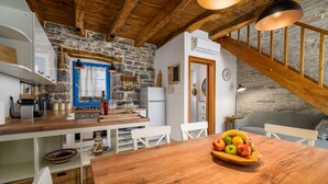 Una cocina rústica con paredes de piedra, vigas de madera y una mesa de comedor de madera con fruteros.