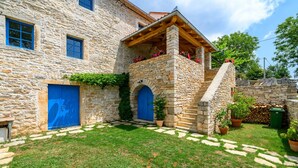 Un edificio de piedra con un porche de madera, dos puertas azules y una pequeña escalera que lleva a un segundo nivel.