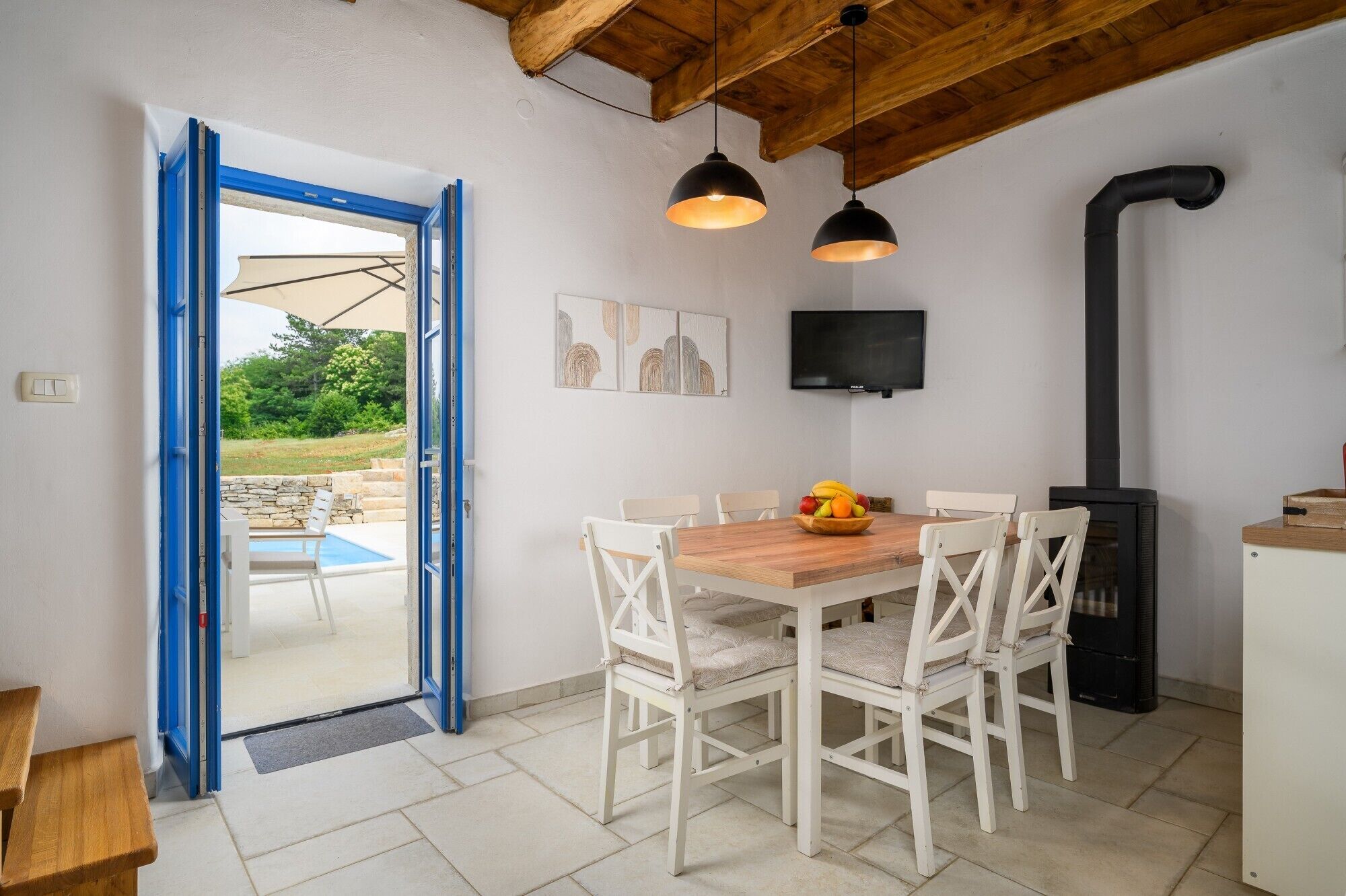 A dining area with a wooden table and white chairs, a black stove, and a TV mounted on the wall.