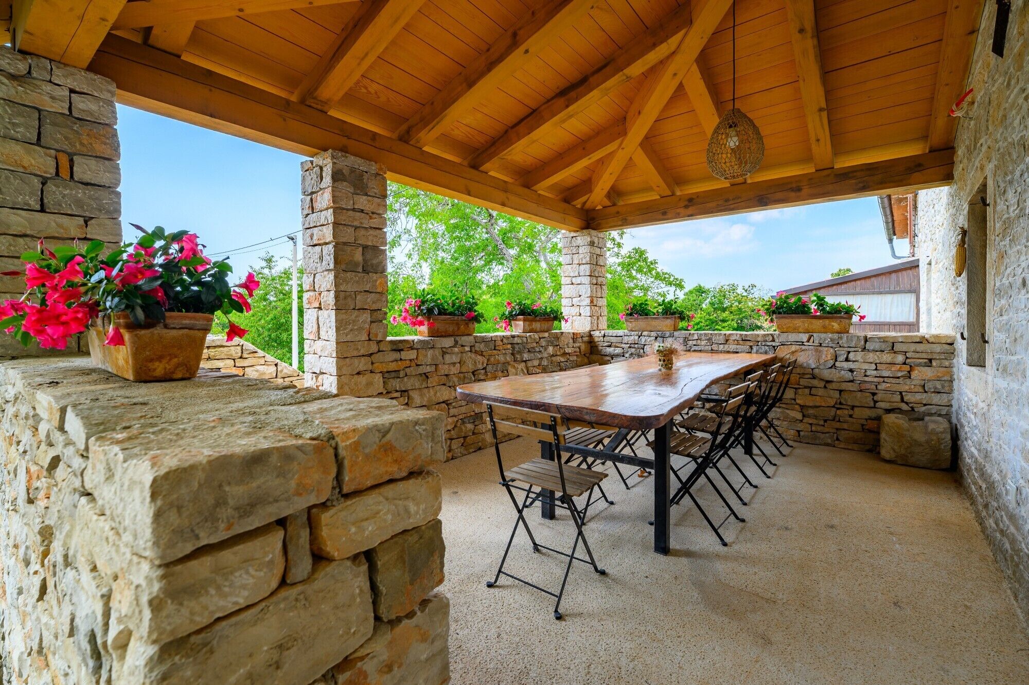 An outdoor patio with a wooden table and chairs, surrounded by stone walls and potted plants.