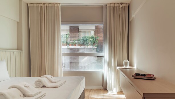 A hotel room with a bed, a bedside table, and a window with curtains.