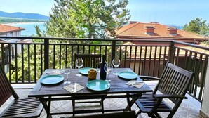 A balcony with a table set for two, overlooking a beach and mountains.
