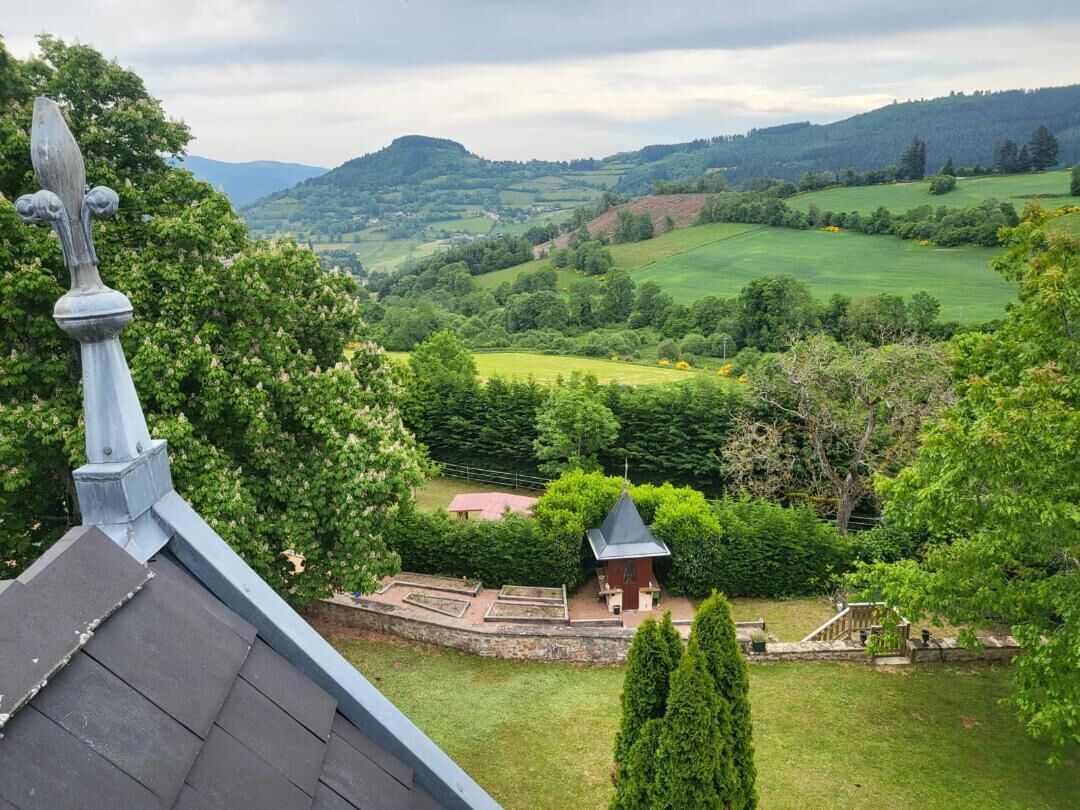 A view of a lush green landscape with rolling hills, a small building with a pointed roof, and a chimney.