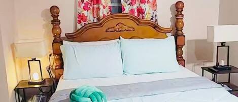 A neatly made bed with a floral bedspread, a green towel, and a wooden headboard.
