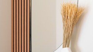 A white vase with dried plants on a black shelf against a wall with vertical wooden slats. - Modern Room Exarchia Room 4 (Αθήνα)