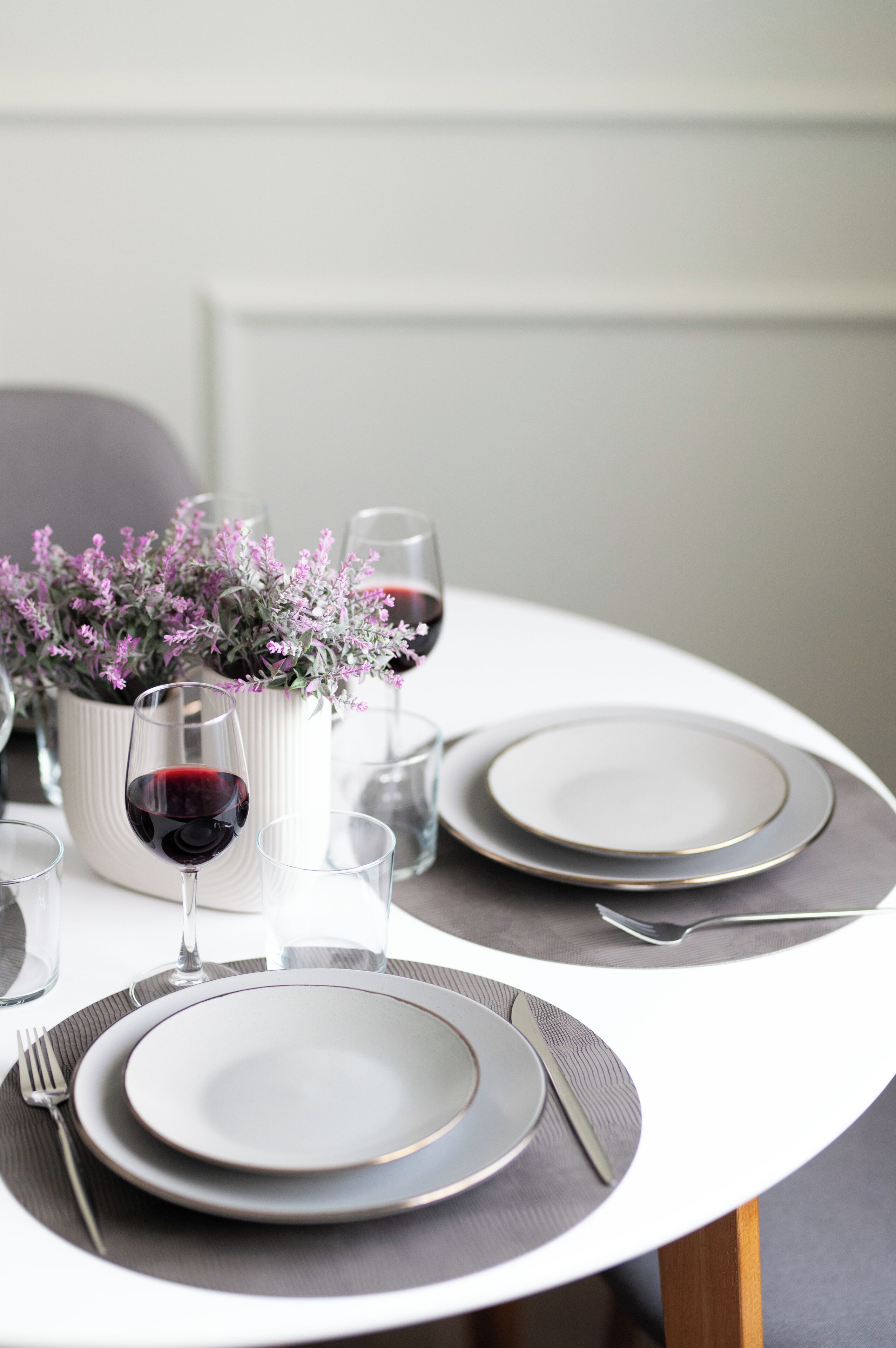 Une table à manger dressée avec des assiettes, des couverts et des verres, agrémentée d’une plante en pot.
