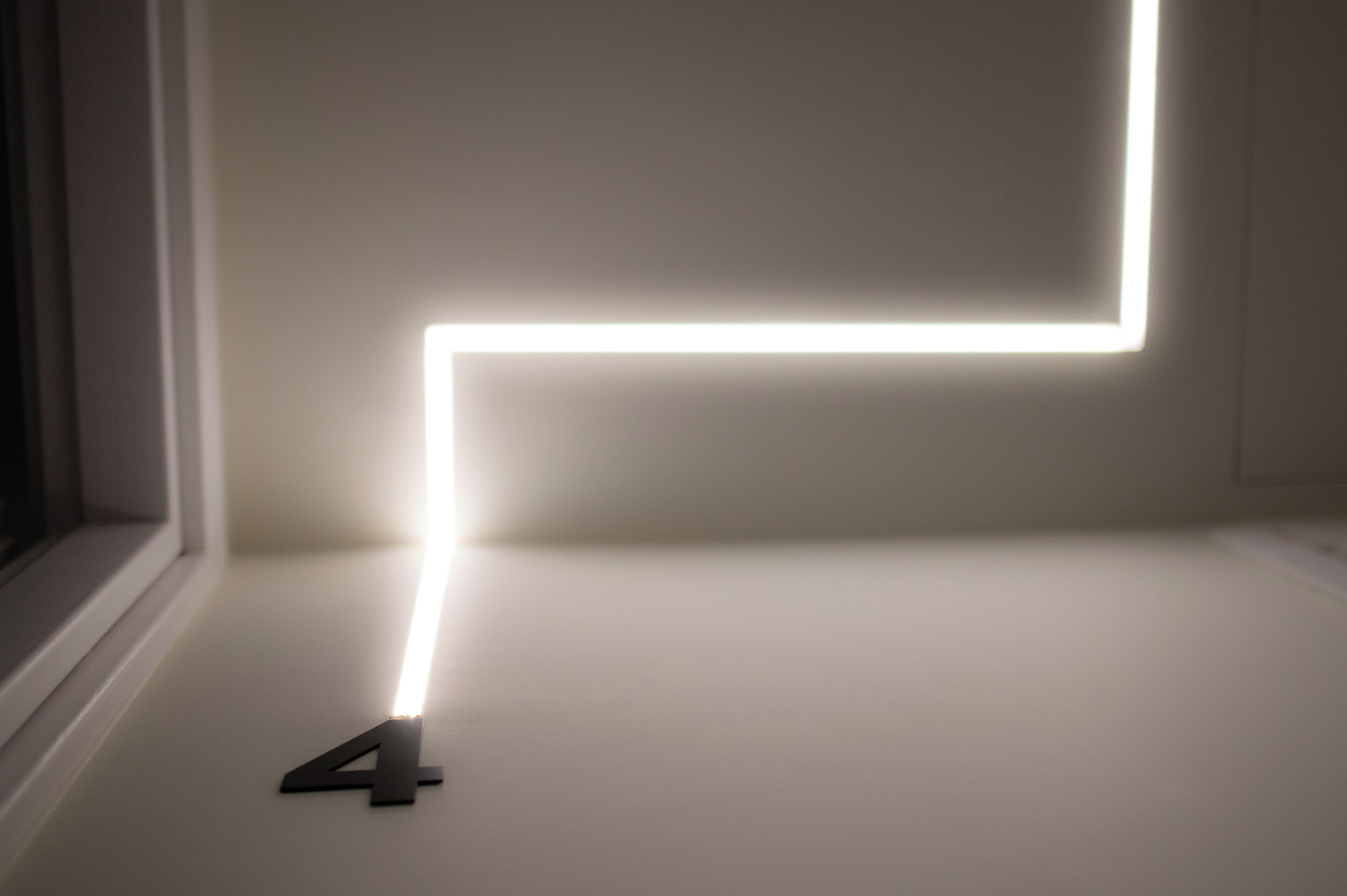 A minimalist room with a white wall and a single light strip forming a geometric pattern.