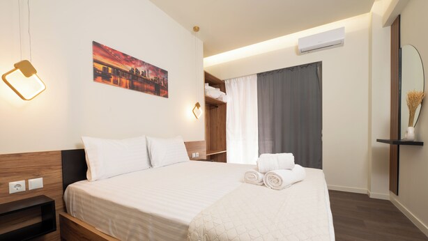 A neatly made bed with a quilted blanket, a bedside table, a wall-mounted light, a painting, a wardrobe, and a mirror. - Modern Room Exarchia Room 4 (Αθήνα)