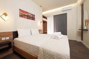 Een netjes opgemaakt bed met een gewatteerde deken, een nachtkastje, een wandlamp, een schilderij, een garderobe en een spiegel.