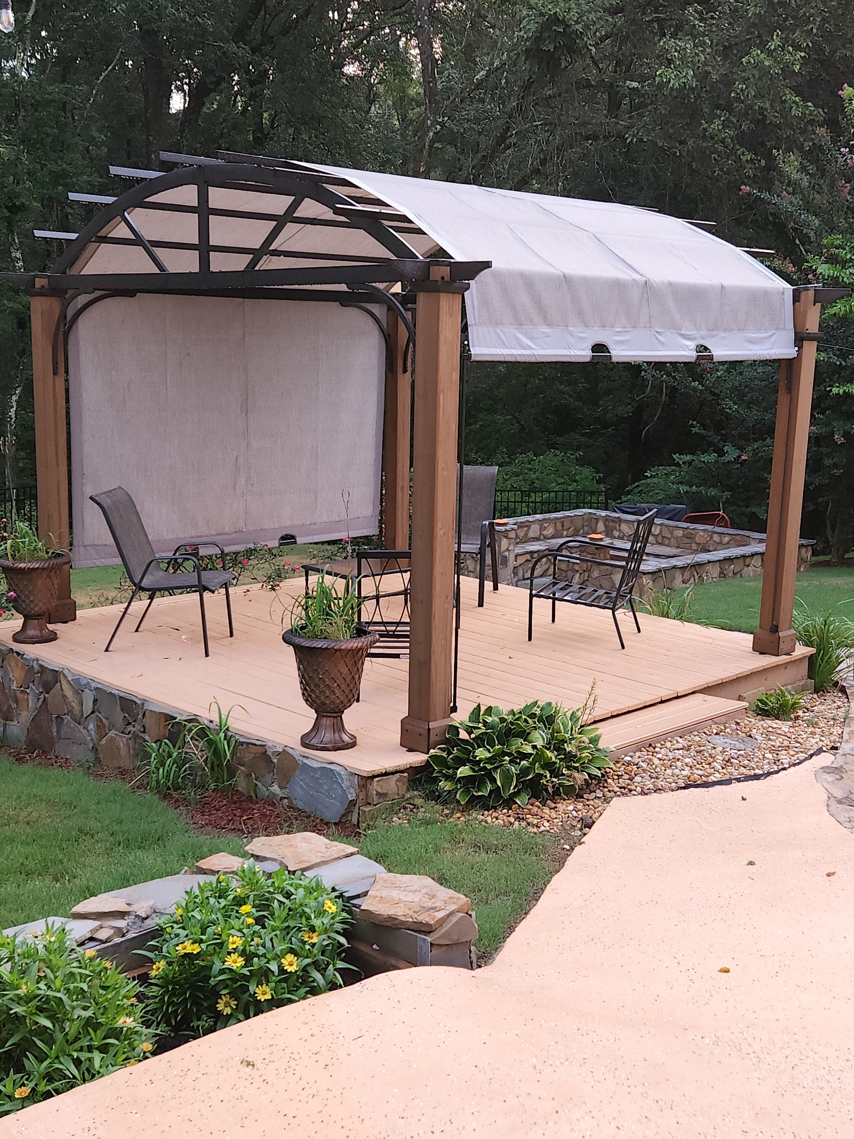 Eine überdachte Terrasse mit einer Pergola, Sitzgelegenheiten im Freien und einer Steinmauer.