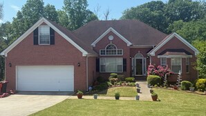 A two-story brick house with a white garage door, a front entrance with a door and windows, and a small front yard with potted plants and a pathway. - FIFA Ready! Spacious 1800 sqf (Ellenwood)