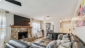 A modern living room with a stone fireplace, leather sofas, and a kitchen in the background. - Relaxing Modern Home Sleeps 6/Pool/BBQ/Firepit (Sorrento)