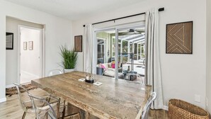 A spacious dining area with a large wooden table, clear glass chairs, and a view of a patio with outdoor seating. - Relaxing Modern Home Sleeps 6/Pool/BBQ/Firepit (Sorrento)