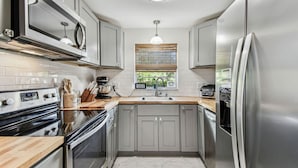 A modern kitchen with stainless steel appliances, a wooden countertop, and a window with blinds. - Relaxing Modern Home Sleeps 6/Pool/BBQ/Firepit (Sorrento)