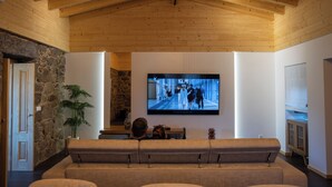 Kodikas olohuone, jossa on suuri taulutelevisio seinällä, kivestä tehty korosteseinä ja puinen katto.
