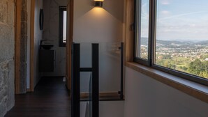 Kapea käytävä, jossa on puupalkkeja, kiviseinä ja ikkuna, josta avautuu näkymä kaupunkiin.
