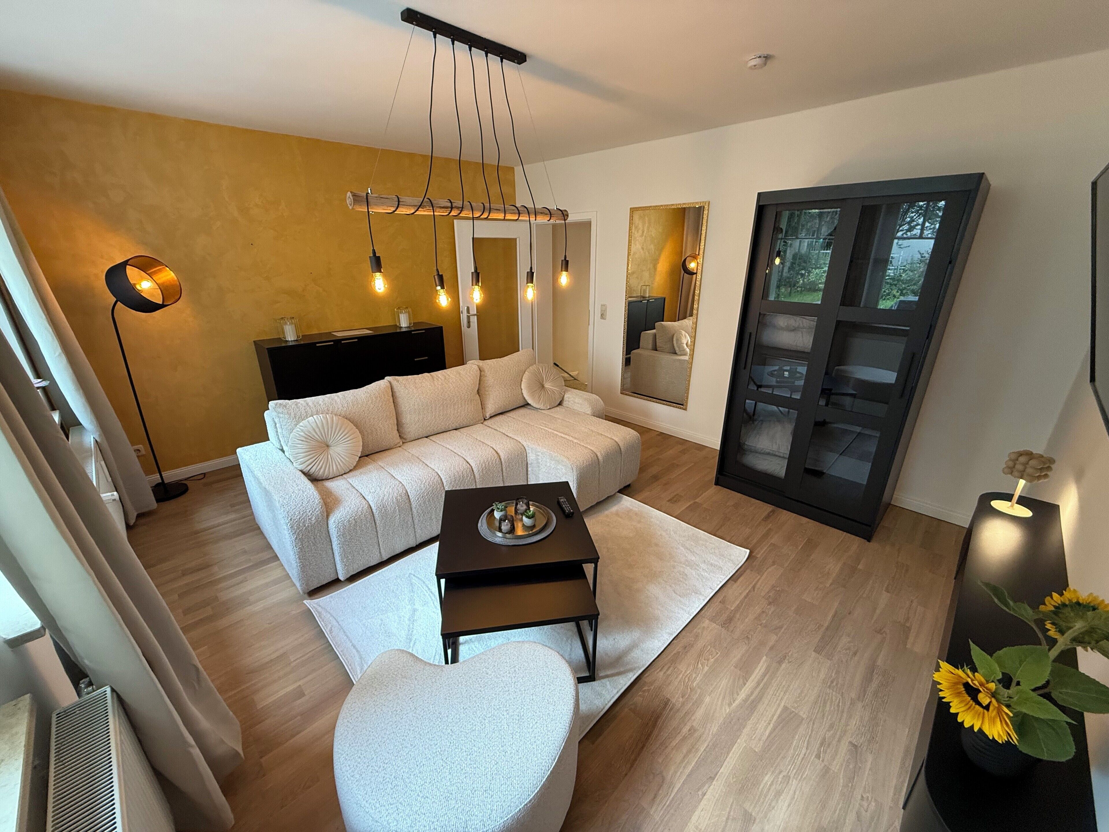 Una sala de estar moderna con un sofá, una mesa de centro y una lámpara de pie. Hay un espejo grande y una puerta corredera que da a otra habitación.
