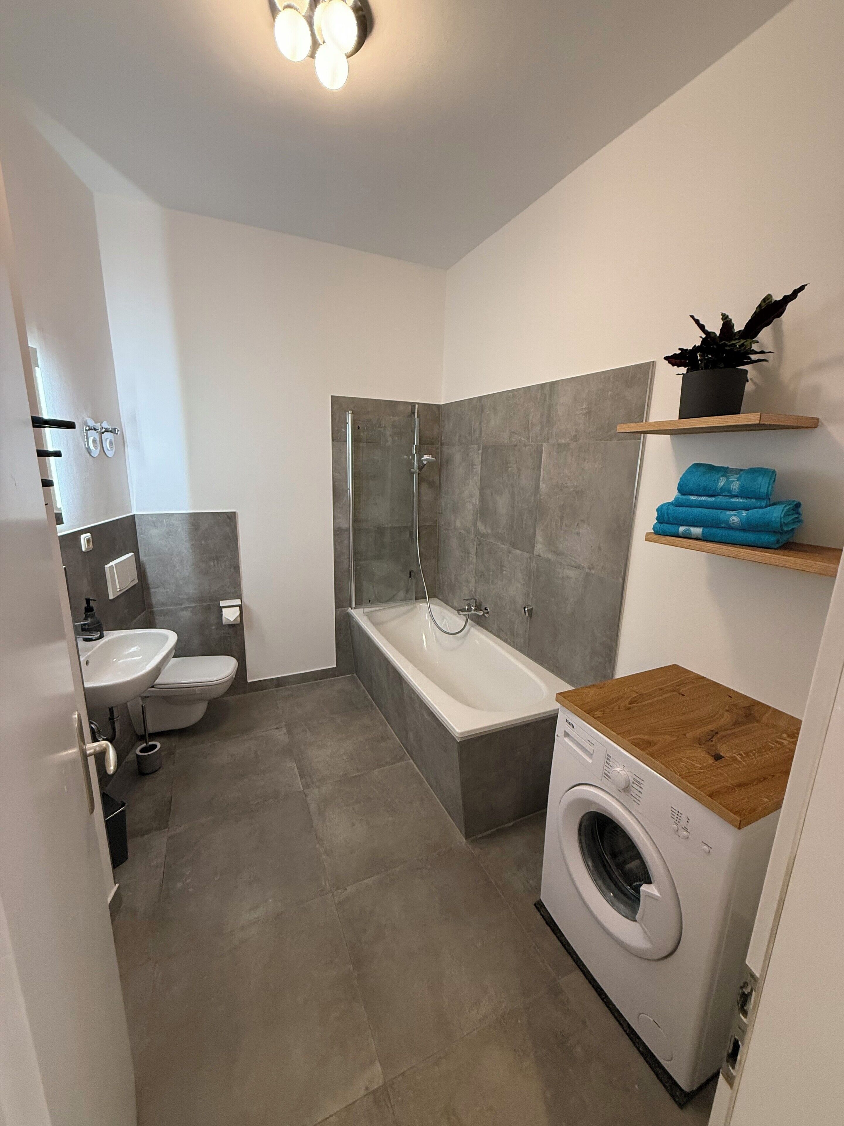 Une salle de bain moderne équipée d’une douche, de toilettes, d’un lavabo et d’un lave-linge encastré.