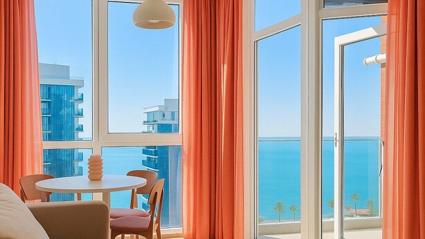 A modern living room with a sofa, a dining table with chairs, and large windows with orange curtains. - Chic 1-bedroom apartment in charming Batumi with AC, WiFi (Batumi)