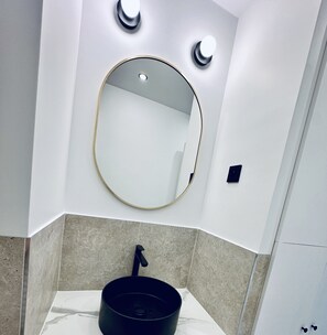 A bathroom with a round mirror, a black sink, and two wall-mounted lights.