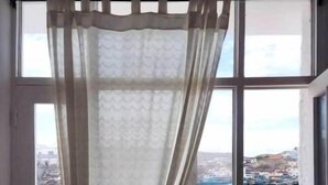 Une fenêtre avec un rideau léger et une vue sur une étendue d’eau et des bâtiments.