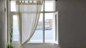 Une petite pièce avec un lit, une fenêtre donnant sur la mer et une plante en pot.