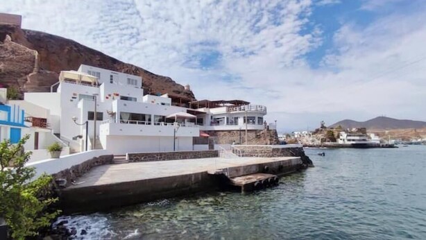Un bâtiment situé sur la côte, doté d’une terrasse donnant sur le front de mer et d’une colline rocheuse en arrière-plan.
