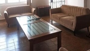 Een ruime woonkamer met een salontafel met glazen blad, twee banken en een groot raam met roedeverdeling.