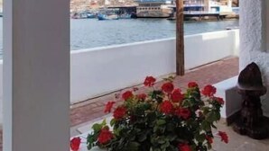 Een balkon met een bloemenarrangement in een pot, een hanglamp en een uitzicht op boten op het water.