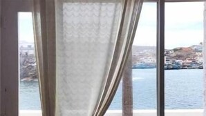 Ett fönster med en tunn, genomskinlig gardin och utsikt över en kuststad.