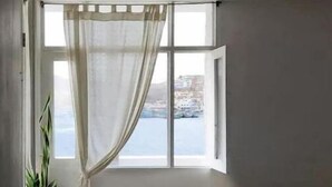 Ett litet rum med en säng, ett fönster med utsikt över havet och en krukväxt.