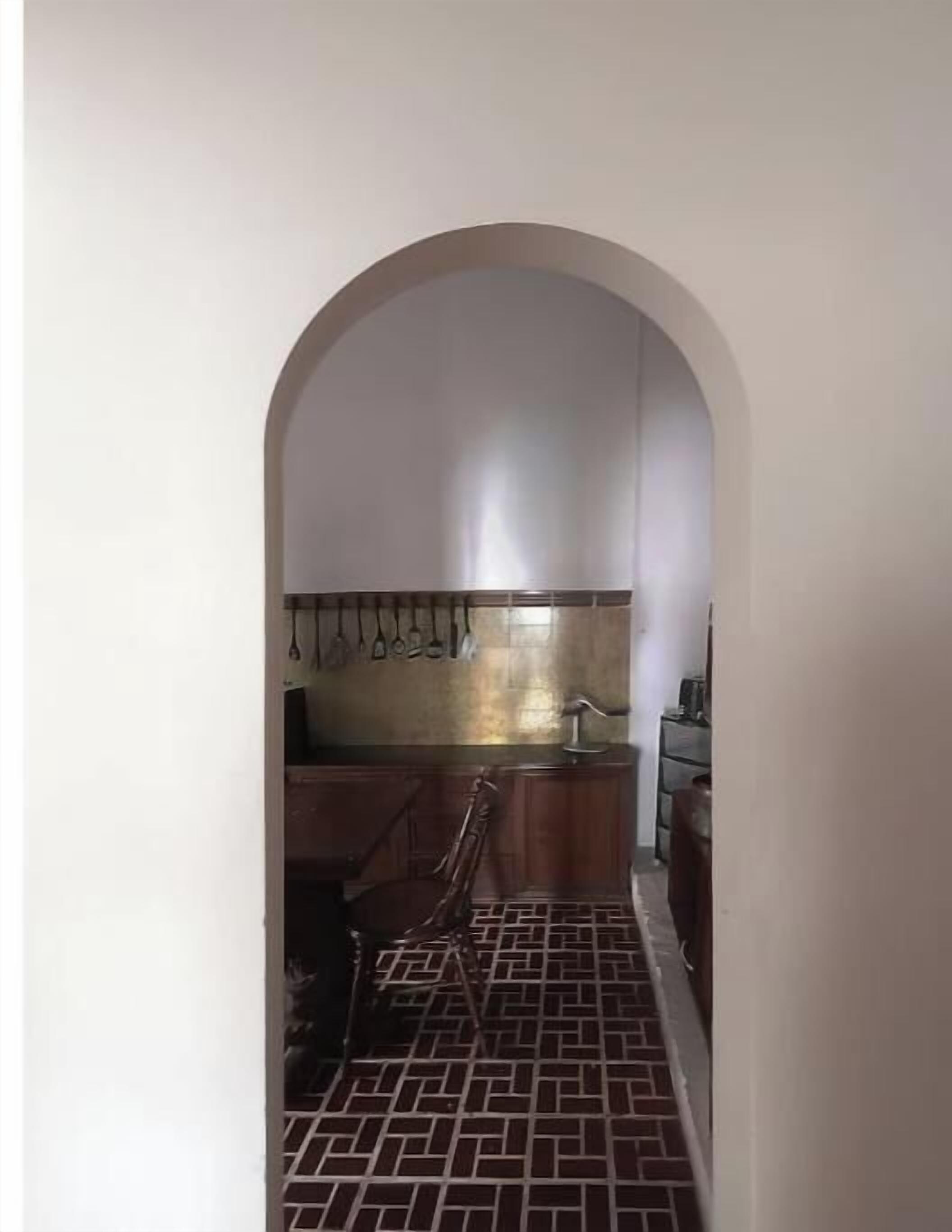 A narrow hallway leading to a kitchen with a tiled floor and a hanging rack.