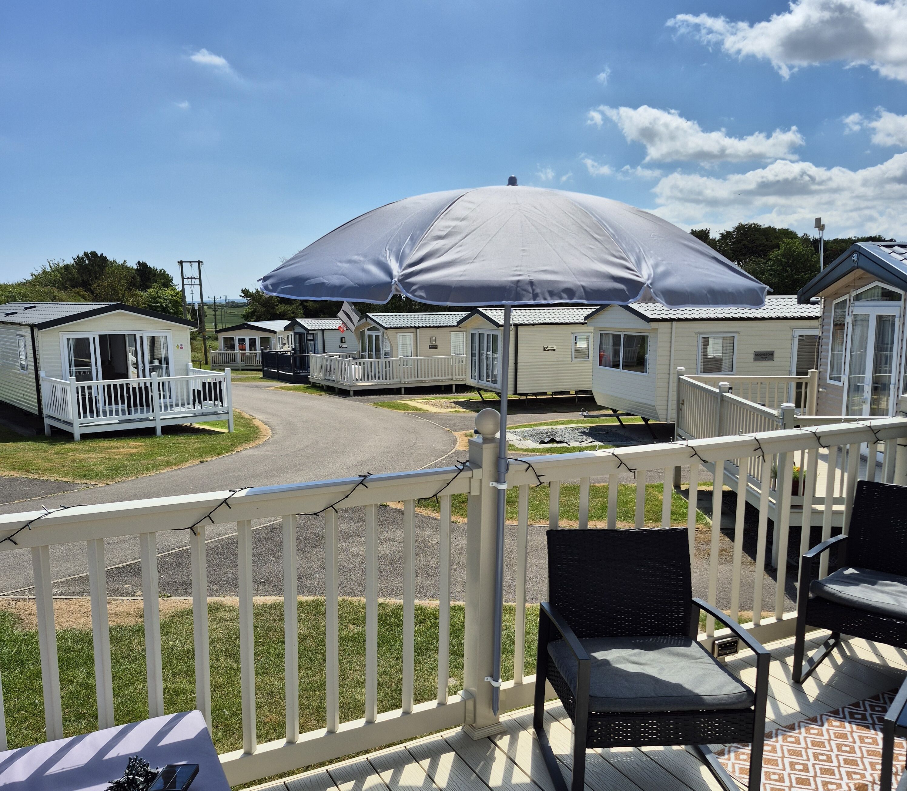 A mobile home with a covered patio area, a white fence, and a grassy lawn.