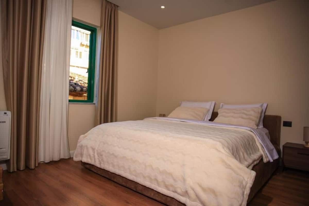 A bedroom with a bed, curtains, a window, and a nightstand.