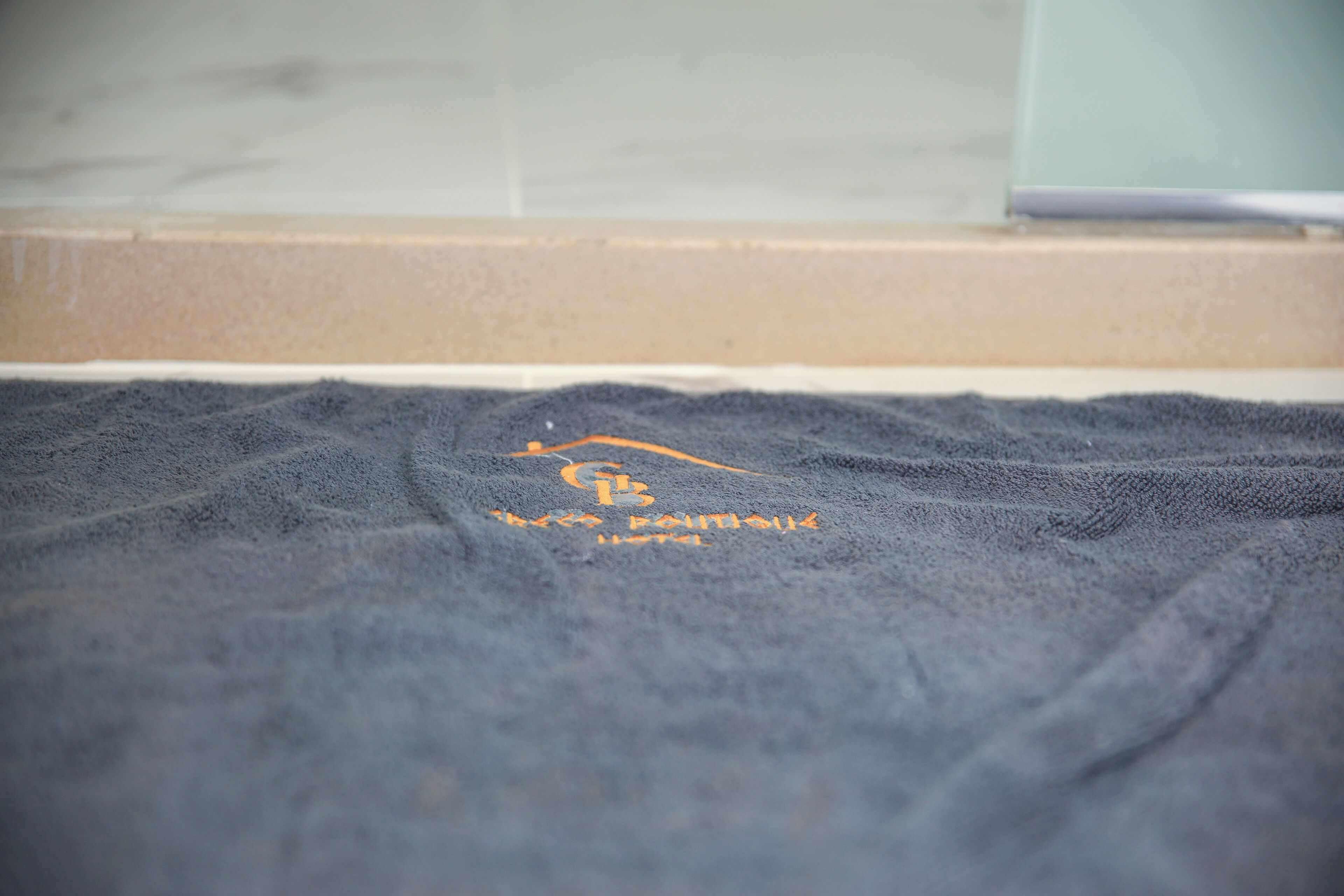 Une serviette bleu foncé, ornée d’un logo et d’un texte, est posée sur le sol d’une salle de bain.