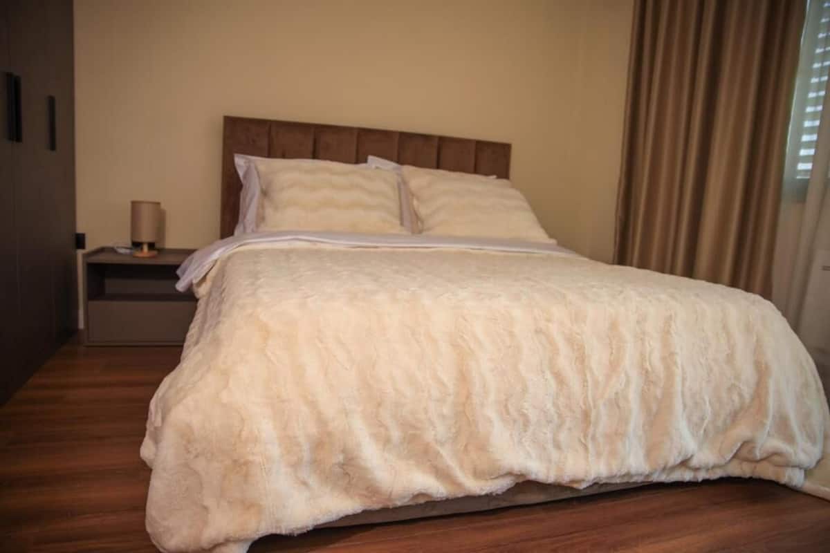 A neatly made bed with a fluffy white duvet, a wooden headboard, and a bedside table with a lamp.