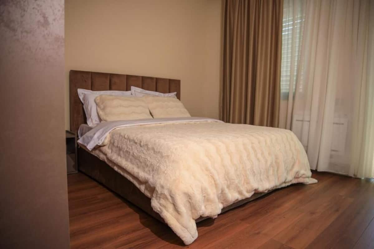 A bedroom with a wooden bed, beige bedding, and a window with curtains.