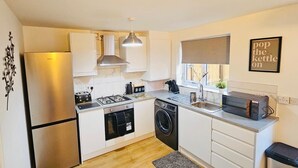 Una cocina compacta con armarios blancos, un refrigerador de acero inoxidable, estufa a gas, microondas y lavadora.