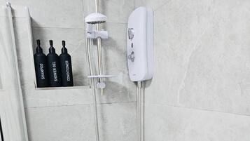 A bathroom with a bathtub, a shower, and a shelf with three bottles labeled shampoo, shower gel, and conditioner.