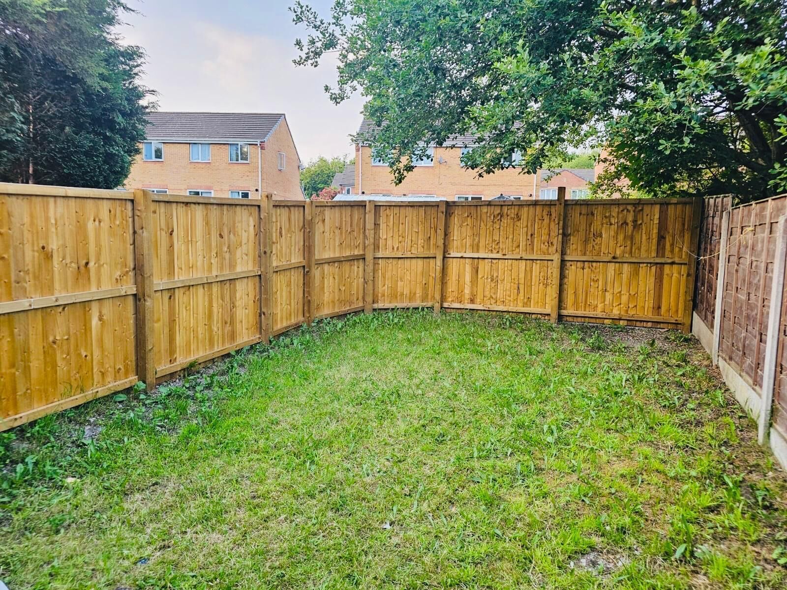 A fenced backyard with grass and a brick building in the background.