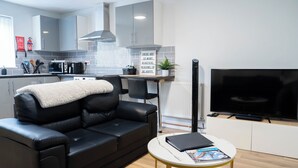 Ein modernes Wohnzimmer mit einem schwarzen Ledersofa, einem Flachbildfernseher und einem kleinen runden Tisch mit Zeitschriften.