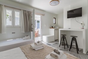 A modern hotel room with a bed, a desk with a TV, a bathroom, and a view of the outside.