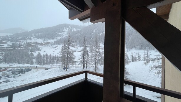 A snow-covered mountain landscape viewed from a balcony with wooden beams and a metal railing. - Fully renovated duplex apartment at the foot of the slopes. (Allos)