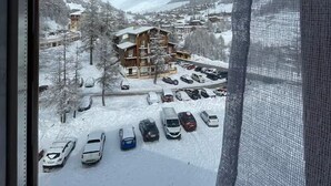 A view of a building with a parking lot in front, surrounded by snow-covered trees and mountains. - Fully renovated duplex apartment at the foot of the slopes. (Allos)