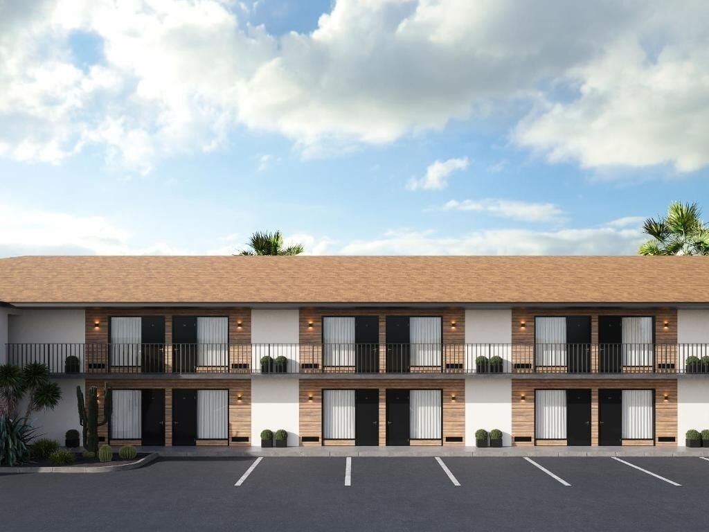 A two-story motel with a flat roof, multiple balconies, and a parking lot in front.