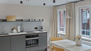 A modern kitchen with grey cabinets, a white countertop, and a dining area with a white table and chairs. - Apartment 7 Lemon (Lüneburg)
