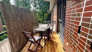 Une terrasse en bois avec une table et des chaises, un mur en briques et une clôture en bambou.