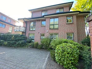 A multi-story brick building with a paved driveway, multiple windows, and a balcony.